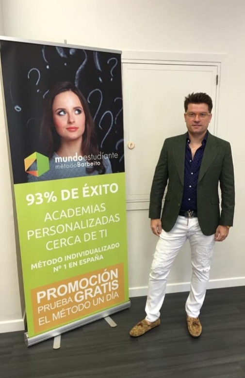 Antonio Barbeito con pantal´pon blanco y americana gris, posando junto a una cartel de academias