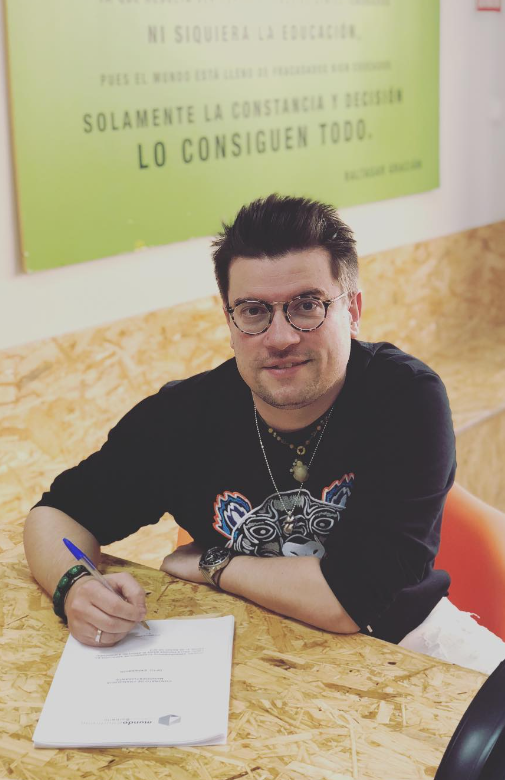 Antonio Barbeito sentado firmando un documento sobre una mesa de madera